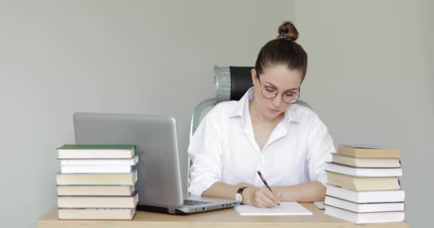 Lány egyetemi hallgató tanul és ír esszét jegyzetfüzetbe az asztalnál. — Stock videók