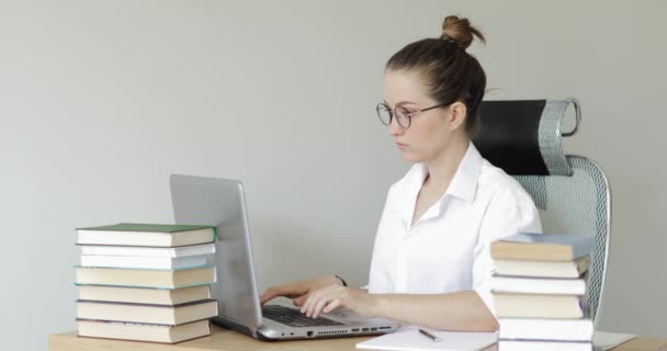 Estudante mulher concentrada estudando e digitando no laptop à mesa entre os livros . — Vídeo de Stock