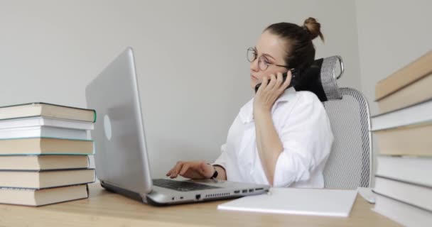 Dizüstü bilgisayarda çalışan ve akıllı telefondan konuşan kız öğrencinin portresi. — Stok video