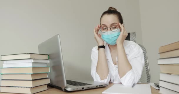 Уставшая студентка в медицинской маске сидит в библиотеке кампуса и пытается учиться. . — стоковое видео
