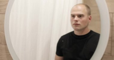 Yorgun genç adam sabah banyoda aynaya bakıyor ve yüzünü yıkıyor..