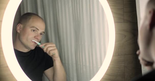 Mannen borstar tänderna tittar på spegeln i badrummet, munhygien koncept. — Stockvideo