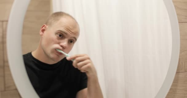 Reflexión en el espejo del hombre que se cepilla los dientes en el baño por la mañana. — Vídeo de stock