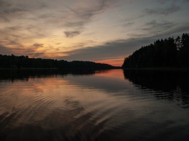 Gölde gün batımı. güzel renkler. kaotik bulutlar. Parlama. siyah orman silueti. Vaidava Gölü, Letonya