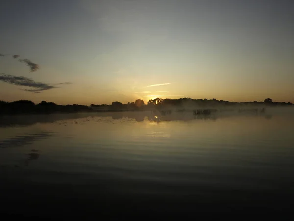 foggy blured orange sunrise at a river, the burning sky is reflected in calm water , dark tree silhouettes, Salaca river, Burtnieks lake, Latvia