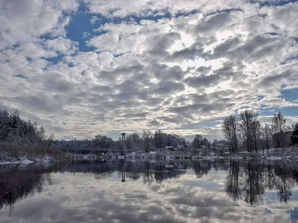 view of beautiful river winter day, snowy trees, many clouds, beautiful reflections, calm river water, Gauja river, Valmiera, Latvia