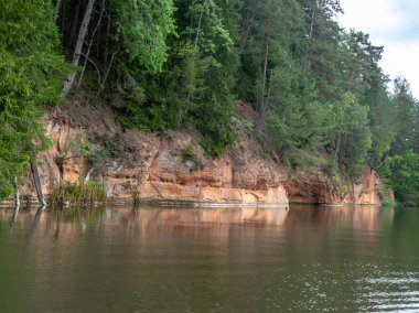 güzel kumtaşı kayalıklar, yeşil ağaçlar, su yansımaları, Brasla nehri, Letonya ile manzara
