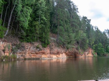 güzel kumtaşı kayalıklar, yeşil ağaçlar, su yansımaları, Brasla nehri, Letonya ile manzara