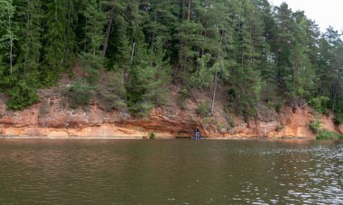 güzel kumtaşı kayalıklar, yeşil ağaçlar, su yansımaları, Brasla nehri, Letonya ile manzara