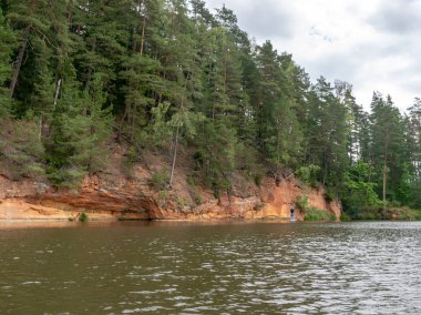 güzel kumtaşı kayalıklar, yeşil ağaçlar, su yansımaları, Brasla nehri, Letonya ile manzara