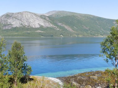 Arka planda dumanlı dağlar ve ön planda mavi su olan manzara, güzel bulanık bir parıltı.