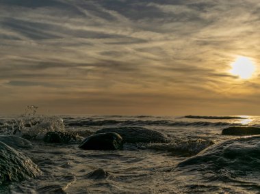 Mavi saat boyunca gün batımından sonra Baltık Denizi üzerinde odaklanmış bulutlar, doğal kayalar, uzun süre suda bulanık yansımalar.