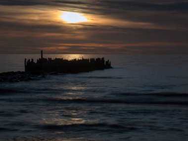 Denizin üzerinde çözünmüş güzel dramatik gökyüzü, arka planda taş iskelesi, günbatımında yansıma, uzun pozlama 