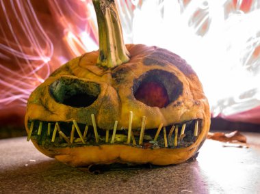 Korkunç oyulmuş balkabağı ve arka planda renkli çizimler, Cadılar Bayramı için uygun.