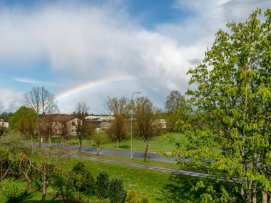 Ağaçların üzerinde gökkuşağı olan güzel renkli bir manzara, küçük bir köy manzarası.