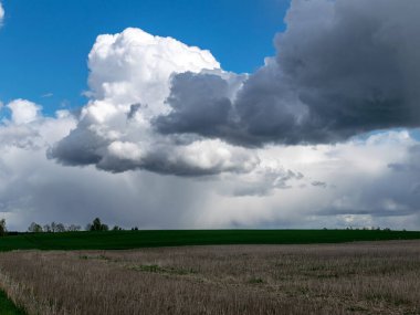 Gri tarlalardan ve yeşil otlardan gelen bahar kırsal arazisi kümülüs ve yağmur bulutlarıyla dolu yüksek mavi gökyüzü.