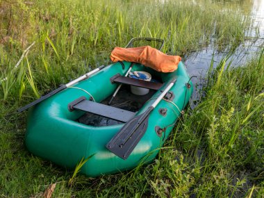 Göl kıyısında yeşil lastik bir teknesi olan yaz manzarası, balık tutma araçları