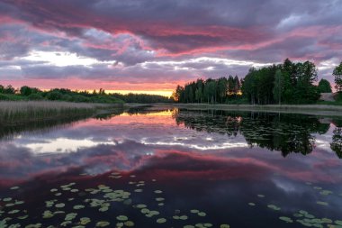 Günbatımı bulutları gölün sakin ayna suyuna yansıyor. Arka planda gölün yansımaları olan güzel bir gün batımı.