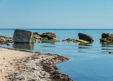 Kayalık bir deniz kıyısına sahip güneşli yaz manzarası, sudaki eski beton bir yapının kalıntıları, Saaremaa Adası, Sorves Yarımadası, Estonya
