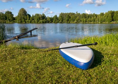 Güneşli yaz manzarası, ön planda yiyecek panosu, yeşil göl kıyısı, yaz zamanı.