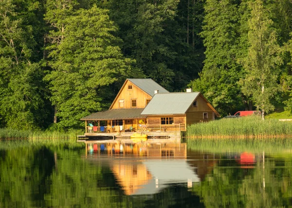 Göl kenarındaki yeşil manzara, göl kenarındaki güzel ahşap ev, durgun suda yansımalar, yaz zamanı.