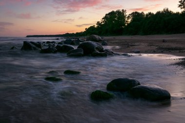Güneş doğmadan önce kayalık deniz kıyıları, karanlık taş siluetleri ve renkli gökyüzü, Baltık Denizi kıyıları, Letonya