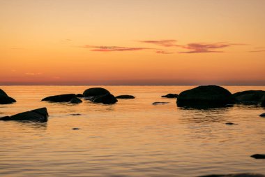 Deniz kenarında turuncu gün batımı, deniz zemininde siyah taş siluetler, yaz akşamı