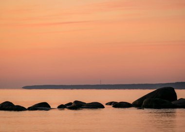 Deniz kenarında turuncu gün batımı, deniz zemininde siyah taş siluetler, yaz akşamı