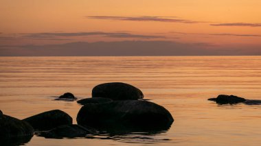 Deniz kenarında turuncu gün batımı, deniz zemininde siyah taş siluetler, yaz akşamı