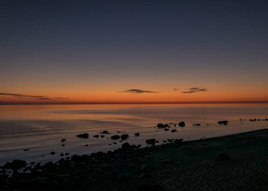 Deniz kenarında turuncu gün batımı, deniz zemininde siyah taş siluetler, yaz akşamı