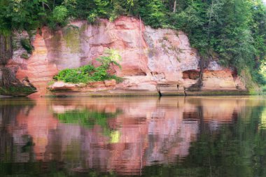 Nehirde güzel bir gün, kumtaşı kayalıkları ve sudaki ağaç yansımaları, mavi gökyüzü nehir suyuna yansıyor, Gauja nehri, Letonya