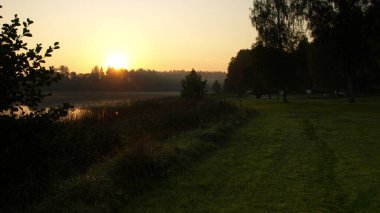 Gölün yanında gün doğumu manzarası, sakin ve sakin bir sabah, çayırda sabah çiyleri, sonbahar bitkileri, Letonya