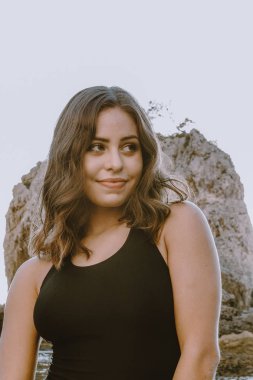 Güzel genç latin kadın kavramı, makyaj olmadan gülümseyerek, yan lara bakıyor. Siyah mayoyla. Denizin önünde olmaktan mutluyum..