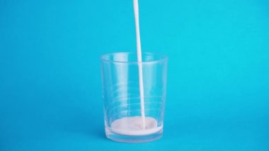 Mavi arka planda bir bardak sütü doldurmak. Dolma kavramı ve kalsiyum açısından zengin. Popüler arkaplanda süt.