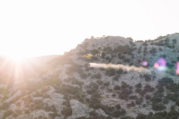 Helicopter of fires throwing water on the mountains at sunset. Firefighter concept and extinguishing fires.