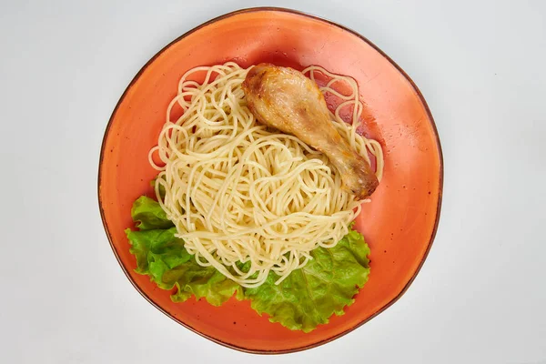 Spagetti ve kızarmış tavuk bacağı. Turuncu tabakta yeşil salata var. Beyaz arkaplan.