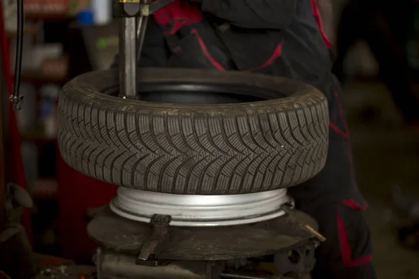 Man changing car tires in garage because of winter season. Fitting tire on rim.