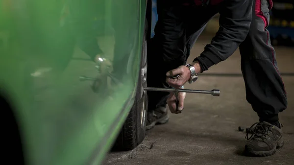 Kış mevsimi yüzünden garajda araba lastiklerini değiştiren adam. Tekerleği vidalama. — Stok fotoğraf