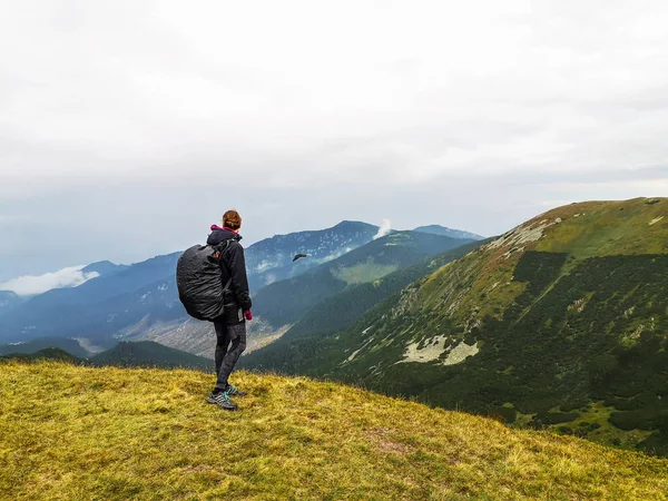 Hiking girl with backpack standing enjoying mountains scenery on rainy day