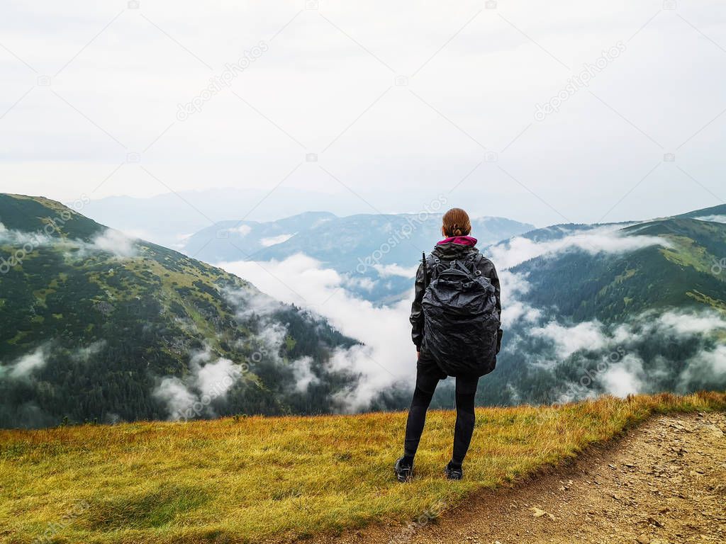 Hiking girl with backpack standing enjoying mountains scenery on rainy day