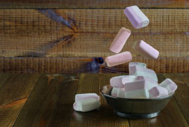 Pembe ve beyaz marshmallow güzel ahşap bir masa üzerinde duran bir tabak üzerine düşüyor