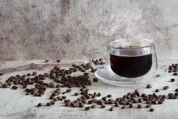 Hot coffee in a beautiful transparent Cup, coffee beans scattered on a gray background