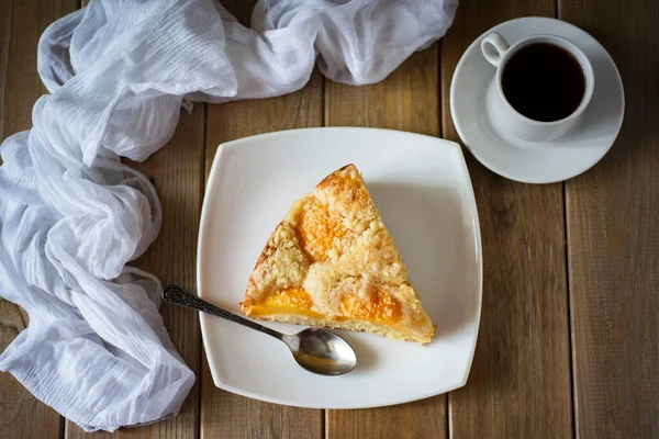 A piece of peach pie on a white plate on a wooden background