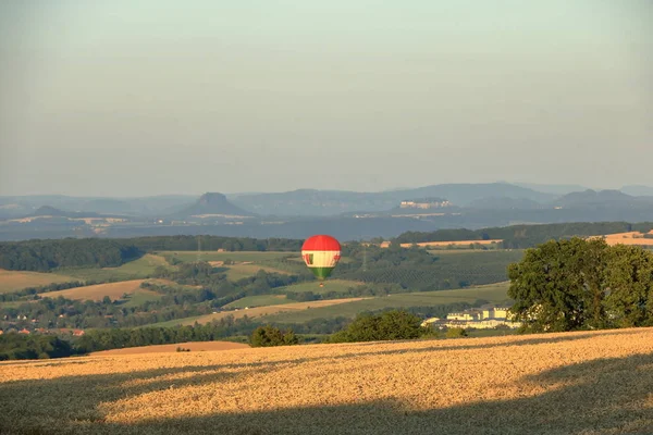 Hot air balloon over the field with blue sky in front of saxony switzerland — Stock Photo, Image