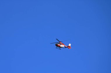 Kırmızı kurtarma helikopteri bulanık pervaneli mavi gökyüzünde ilerliyor.