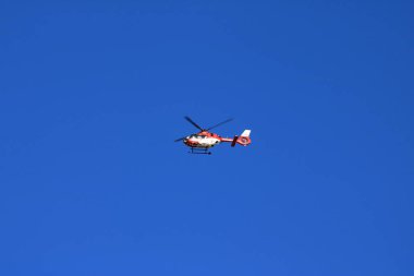 Kırmızı kurtarma helikopteri bulanık pervaneli mavi gökyüzünde ilerliyor.