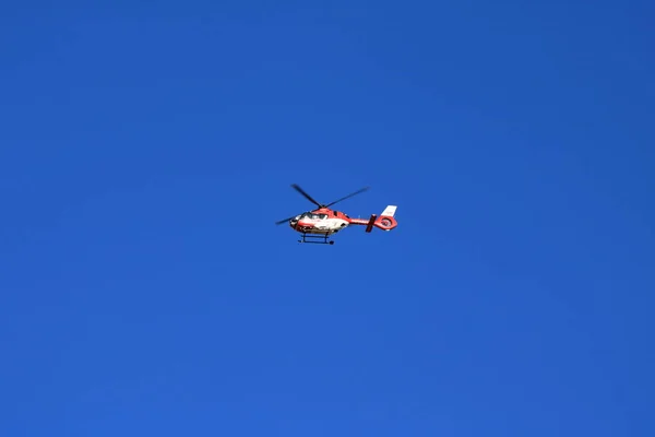 Червоний рятувальний вертоліт рухається в блакитному небі з розмитим пропелером. — стокове фото