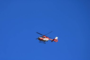 Kırmızı kurtarma helikopteri bulanık pervaneli mavi gökyüzünde ilerliyor.