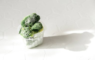 Beyaz zemin üzerinde donmuş brokoli olan plastik torba, üst manzara. Sebze koruma