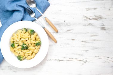 Beyaz masadaki beyaz kasede tahtayı kesen brokolili İtalyan makarnası. Üst Manzara. Boşluğu kopyala.